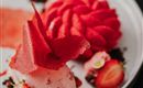 Ein kunstvoll angerichtetes Dessert mit Erdbeersorbet und frischen Erdbeeren. Die Präsentation umfasst auch dekorative Elemente aus Fruchtleder.