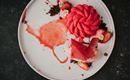 Ein kunstvoll angerichtetes Dessert mit frischen Erdbeeren und einer cremigen Textur. Auf dem Teller sind Schokoladenstückchen und eine fruchtige Sauce zu sehen.