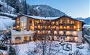 A cozy hotel in the snow, surrounded by mountains. The warm lights create an inviting atmosphere.