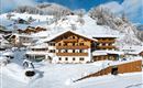 Ein schönes Hotel in einer verschneiten Berglandschaft. Die Umgebung ist winterlich mit schneebedeckten Hügeln und traditionellen Chalets.