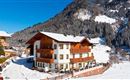 Ein malerisches Chalet inmitten einer verschneiten Landschaft. Im Hintergrund erheben sich schneebedeckte Berge unter einem klaren blauen Himmel.