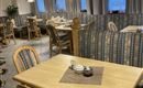 Ein gemütliches Restaurant mit Holztischen und -stühlen. Die Einrichtung ist stilvoll und entspannend, mit großen Fenstern und eleganten Leuchten.