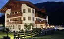 Ein gemütliches Alpenhaus mit mehreren Balkonen, beleuchtet in der Dämmerung. Umgeben von Wiesen und Bergen, strahlt es eine charmante Atmosphäre aus.