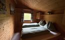 A cozy room with wood paneling and two single beds. Natural light streams through the window and there is a small bucket with plants.