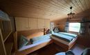 A cozy bedroom with wooden paneling and two beds. The windows offer a view of nature and the room has an inviting atmosphere.