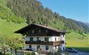 A picturesque house surrounded by green meadows and mountains. The sky is clear and blue.