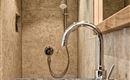 A modern bathroom with an elegant shower and a stylish stone sink. The walls are made of light stone, which gives the room a calm atmosphere.