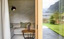 A modern living room with a comfortable couch and an elegant table. Large windows provide a view of the green meadow and the mountains.