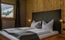 A cozy bedroom with a double bed and wooden paneling. Large windows provide a view of the surrounding nature.