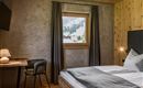 A modern bedroom with a cozy bed and a table. Through the window, one can see the snow-covered mountains.