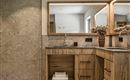 A modern bathroom with wood and stone accents. Two mirrors and an elegant flower vase give the room a stylish ambiance.