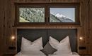 A cozy bedroom with a large bed and pillows. Through the windows, one can see the mountains and the green countryside.