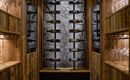 An elegant wooden wine cellar with modern shelves. The wall is adorned with stone, and there are glasses on the shelves.