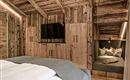 A cozy bedroom with wooden walls and a double bed. A seating area with cushions and a television completes the inviting space.