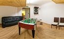 A game room with a foosball table in the center. There is a black sofa and two chairs as well as a dartboard on the wall.