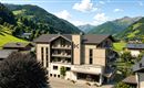 A modern hotel named KATHRIN in the midst of a green mountain landscape. The surroundings show gentle hills and high mountains under a blue sky.