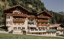 Ein charmantes Hotel im alpine Stil, umgeben von grünen Wäldern. Die Fassade ist mit Holzverkleidungen und Balkonen geschmückt.