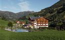 Ein malerisches Hotel inmitten grüner Wiesen und Berge. Im Vordergrund befindet sich ein Schwimmteich und Spielmöglichkeiten für Kinder.