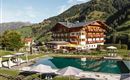 Ein malerisches Hotel in den Alpen mit einem schönen Pool und Liegen. Umgeben von grünen Hügeln und einem klaren blauen Himmel.