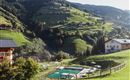 Eine schöne Landschaft mit grünen Hügeln und einem Swimmingpool. Im Hintergrund sind einige Häuser und Bäume zu sehen.