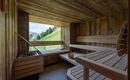 Eine gemütliche Sauna aus Holz mit Blick auf grüne Hügel. Die Bänke sind einladend und die Atmosphäre ist entspannend.