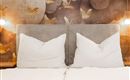 A cozy bed with large, white pillows in front of a stylish wallpaper. The soft lighting creates a relaxed atmosphere.