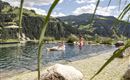 A swimming pool in the mountains with two people in the water. The landscape is green and hilly, under a clear sky.
