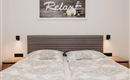 A modern bedroom with a double bed and elegant bedding. A picture with the inscription "Relax" hangs on the wall.