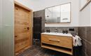 A modern bathroom with a wooden shower door and an elegant wooden sink. The dark tiles and the large mirror wall create a stylish atmosphere.