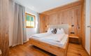 A cozy bedroom with wooden interiors and a large double bed. The window lets in gentle light, creating an inviting atmosphere.