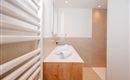 A modern bathroom with a wooden washstand and fresh towels. The walls are light and the lighting is friendly and inviting.