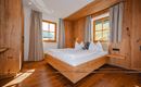 A cozy bedroom with wooden paneling and large windows. The bed is neatly made, and the room feels bright and inviting.