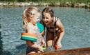 Zwei fröhliche Mädchen spielen im Wasser. Sie tragen Schwimmhilfen und lachen zusammen.