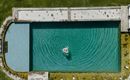 Ein klarer Pool mit blauem Wasser und einem grünem Umfeld. Eine Person schwimmt entspannt in der Mitte des Pools.