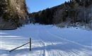 Eine verschneite Landschaft mit einem gefrorenen Weg und dunklen, bewaldeten Bergen im Hintergrund. Der Himmel ist klar und blau, was eine ruhige Winteratmosphäre schafft.