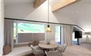 A modern and bright living room with large windows and a cozy seating area. The wooden table invites for social gatherings and offers a view of the green landscape.