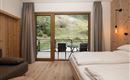 Ein modernes Zimmer mit einem großen Fenster und Blick auf die Natur. Die Einrichtung ist gemütlich mit einem Doppelbett und einer sitzenden Ecke.