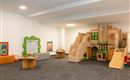 Ein einladender Spielraum mit Holzspielgeräten, Rutschen und einem künstlerischen Bereich. Der Raum ist hell und freundlich gestaltet, ideal für Kinder zum Spielen und Entdecken.