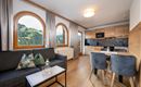 A modern apartment with a cozy seating area and a kitchen. Large windows offer a view of the green mountain landscape.