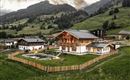 Ein schönes, alpenländisches Haus umgeben von grünen Wiesen und Bergen. Der Garten ist gut gepflegt und von einem Zaun umgeben.