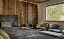 A modern bedroom with a large bed and cozy armchairs. The walls are made of wood and there is a window overlooking nature.