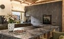 A modern kitchen with wood and concrete accents. On the countertop, there is a vase of flowers and a bowl of nuts.