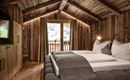 A cozy bedroom with a wooden ceiling and warm light. The room has a large window with a view of the mountains.