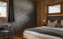 A modern bedroom with wooden details and large windows. There is a comfortable bed and a table with a chair.