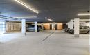 A modern underground parking garage with several parked cars. The lighting is bright and the design is minimalist.