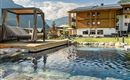 A peaceful garden with a glittering pool and a cozy lounger. In the background stands a modern wooden house in front of a picturesque mountain landscape.