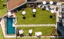A well-maintained garden with a lawn area and several loungers. Next to the garden is a pool and sunny seating areas with umbrellas.