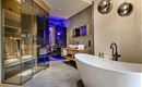 Ein modernes Badezimmer mit einer freistehenden Badewanne und einer Glasduschkabine. Die Wände sind in neutralen Tönen gehalten und es gibt stilvolle Beleuchtungselemente.