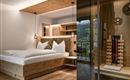 Ein modernes Schlafzimmer mit einem großen Bett aus Holz und klaren Linien. Stilvolle Beleuchtung und eine glasbekleidete Ecke sorgen für ein elegantes Ambiente.