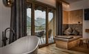 Ein modernes Zimmer mit einer freistehenden Badewanne und einem gemütlichen Sitzbereich. Große Fenster bieten einen Blick auf die Berge.